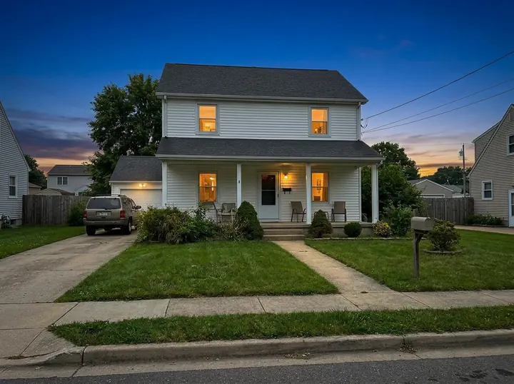 The same white two-story house at twilight with a deep blue sky and warm light in every window