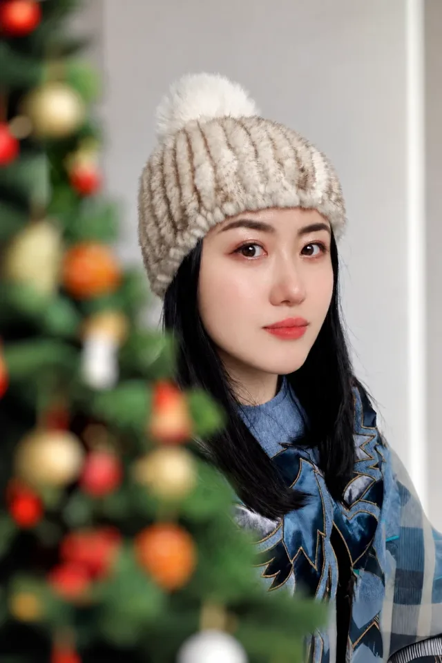The owner's selfie: a woman in a knit beanie with a pompom and a blue scarf, next to a Christmas tree