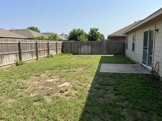 A plain suburban backyard with a patchy lawn, a wooden fence and a small concrete slab by the back door (made with the model)