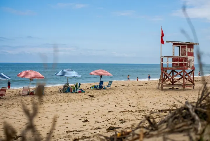 The same beach in true colors: a blue sky with clouds, blue sea, warm sand, striped umbrellas and a red lifeguard tower