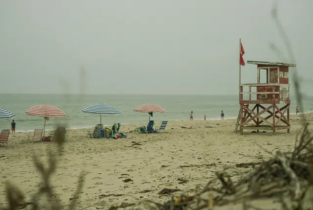 A washed-out beach photo with a green-yellow tint and a hazy gray sky, striped umbrellas and a lifeguard tower (made with the model)