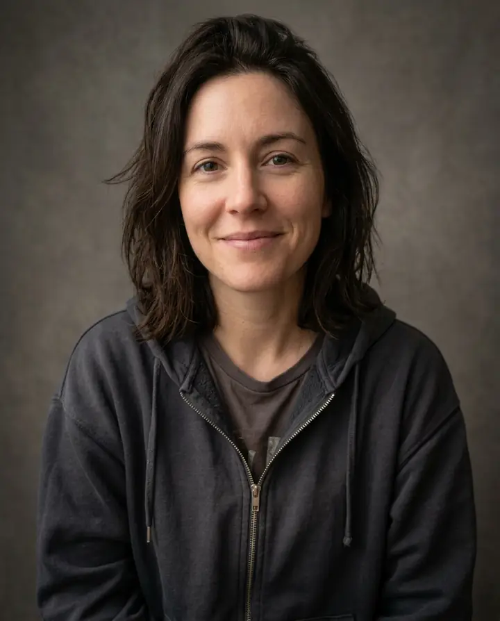 The same selfie retouched: even studio light, clean color and a plain gray backdrop, same face and hoodie