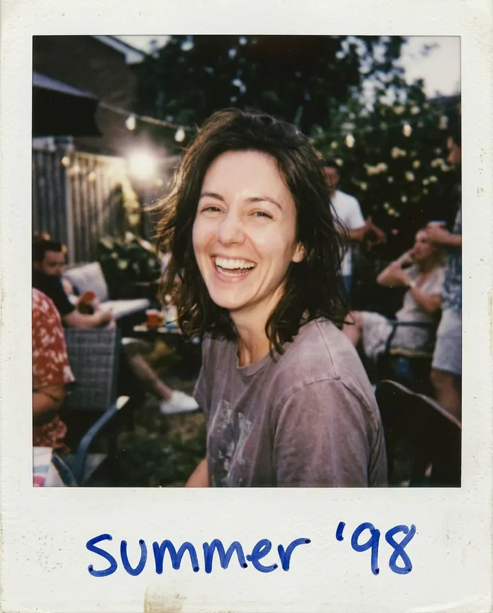 An instant photo of the woman laughing at a backyard party in a white frame with summer '98 written in blue pen