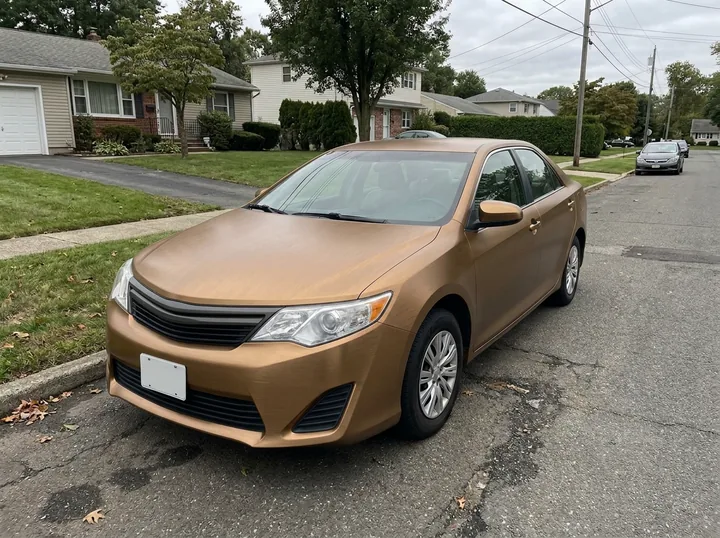 The same sedan in a brushed bronze metal wrap with fine brushed lines on the same street