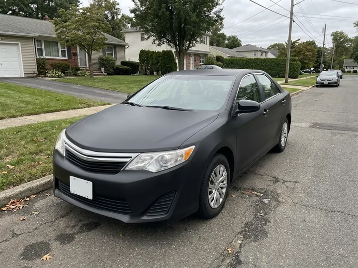 The same sedan in a flat matte black wrap on the same street