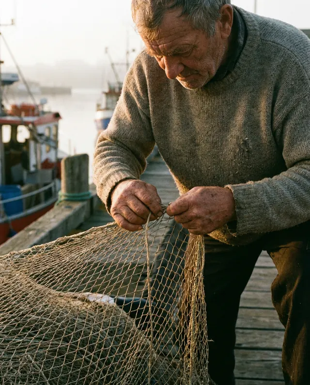Nano Banana Pro: a photo of an elderly fisherman mending a net on a wooden dock at dawn