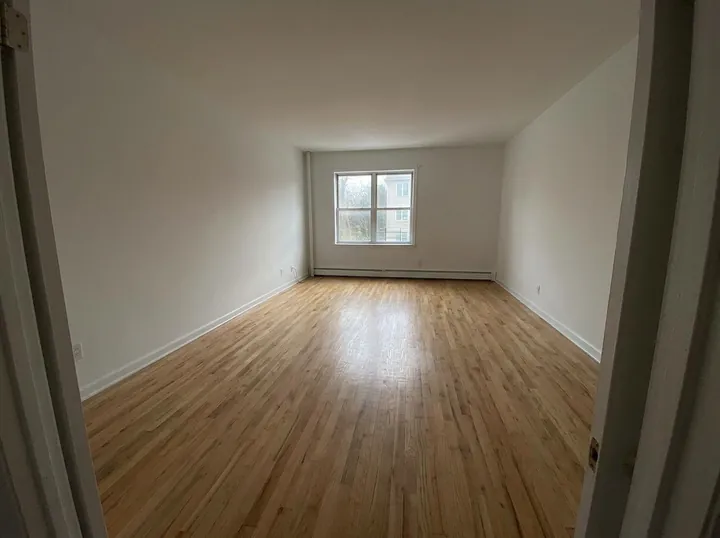 Empty living room with white walls, one window and light oak floors