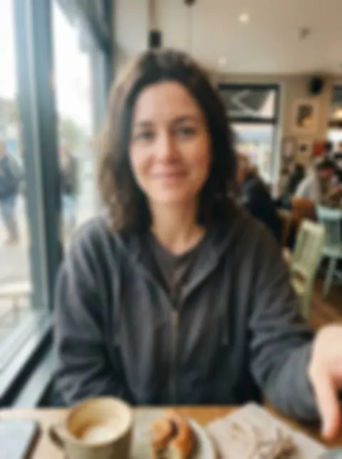A blurry, out-of-focus cafe selfie of a woman in a gray hoodie, 480 pixels wide (a sharp photo made with the model, blurred by us)