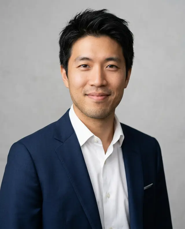 The man in a navy suit and open white shirt against a light-gray studio background