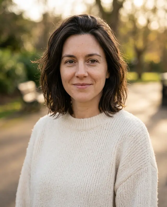 The woman in a cream sweater outdoors with a softly blurred park behind