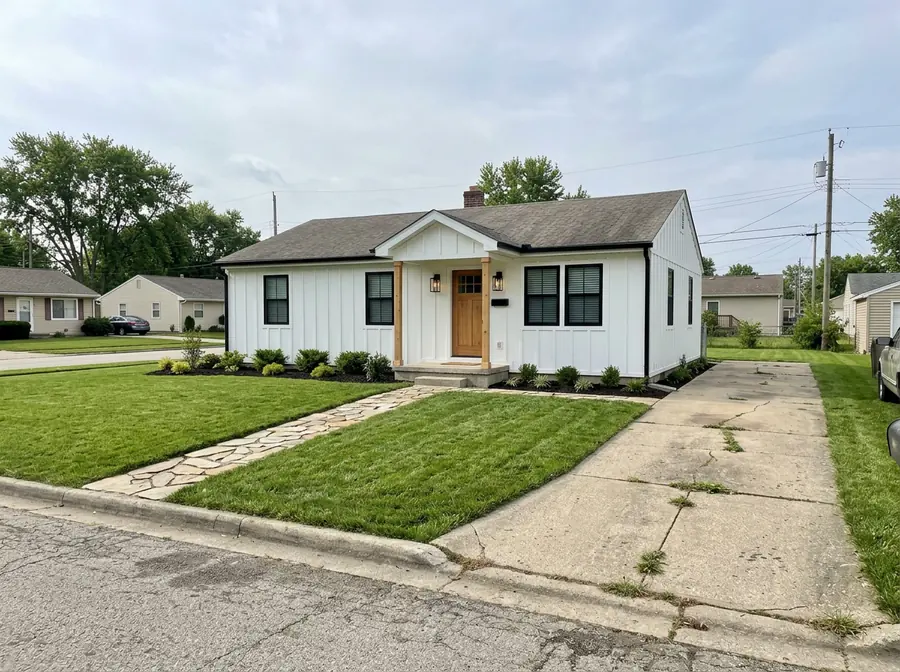 The same one-story house made over in modern farmhouse style: white board-and-batten siding, black windows, wood door and new landscaping