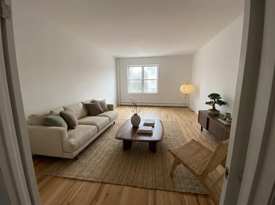 The empty room furnished in Japandi style: a low beige sofa, dark walnut table, jute rug, paper floor lamp and bonsai