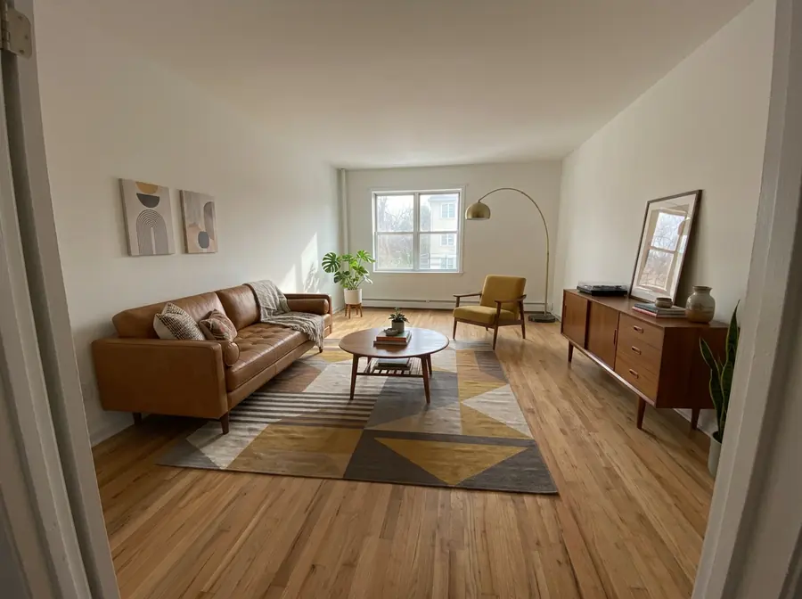 The empty room furnished in mid-century modern style: a caramel leather sofa, teak sideboard, mustard armchair, geometric rug and arc lamp