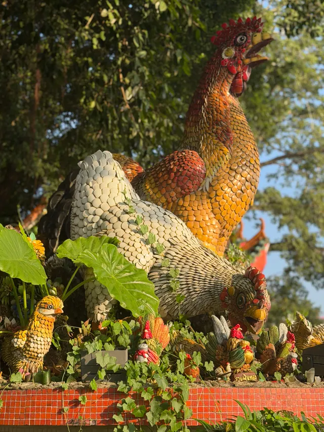 Our own travel photo: giant mosaic statues of a rooster and a hen among leaves and small figurines