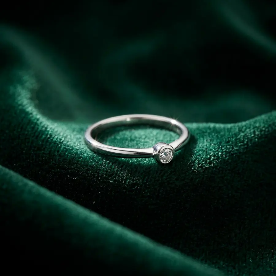 The silver ring with a small clear stone resting on dark green velvet under a soft spotlight