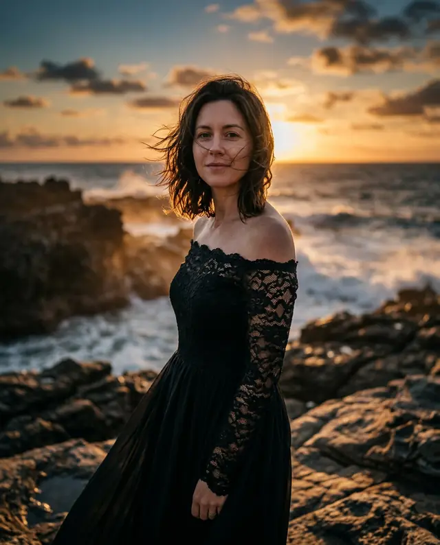 The same woman in a black lace off-shoulder gown on a rocky coast at sunset