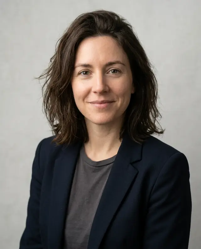 The same woman in a professional headshot with a dark blazer against a light-gray background