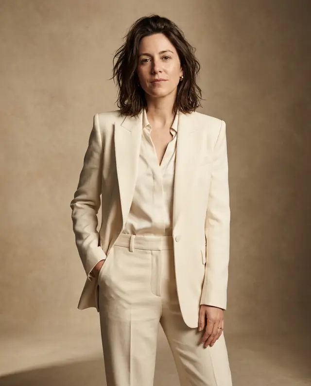 The same woman in a tailored cream suit posing against a warm beige studio backdrop