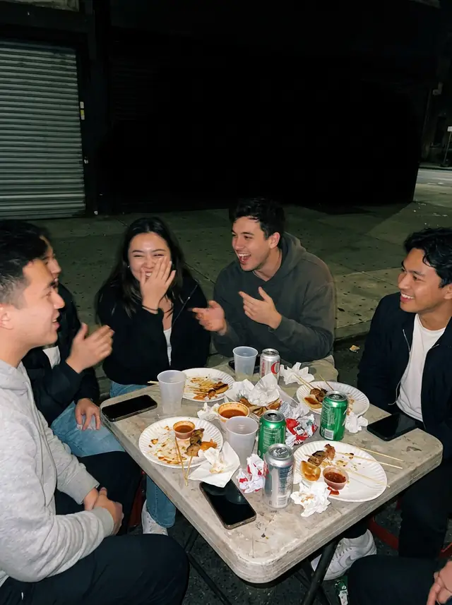 A flash photo at night of friends laughing around a street-food table
