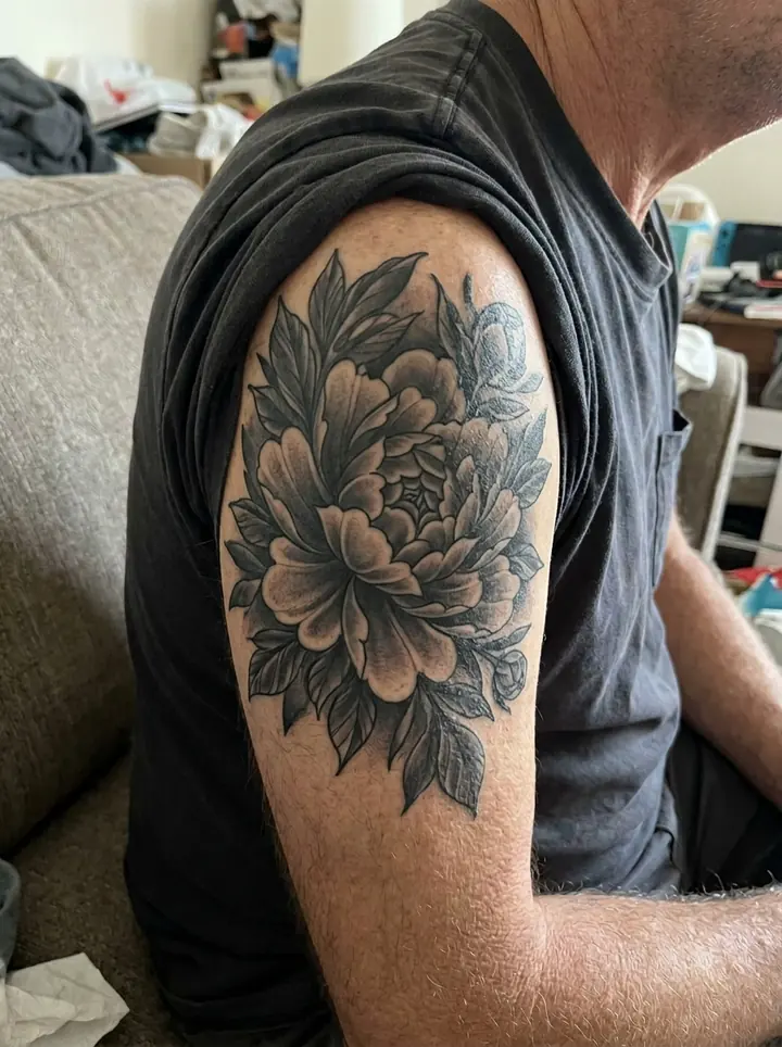 The same arm with a large black and gray peony tattoo covering the old star completely