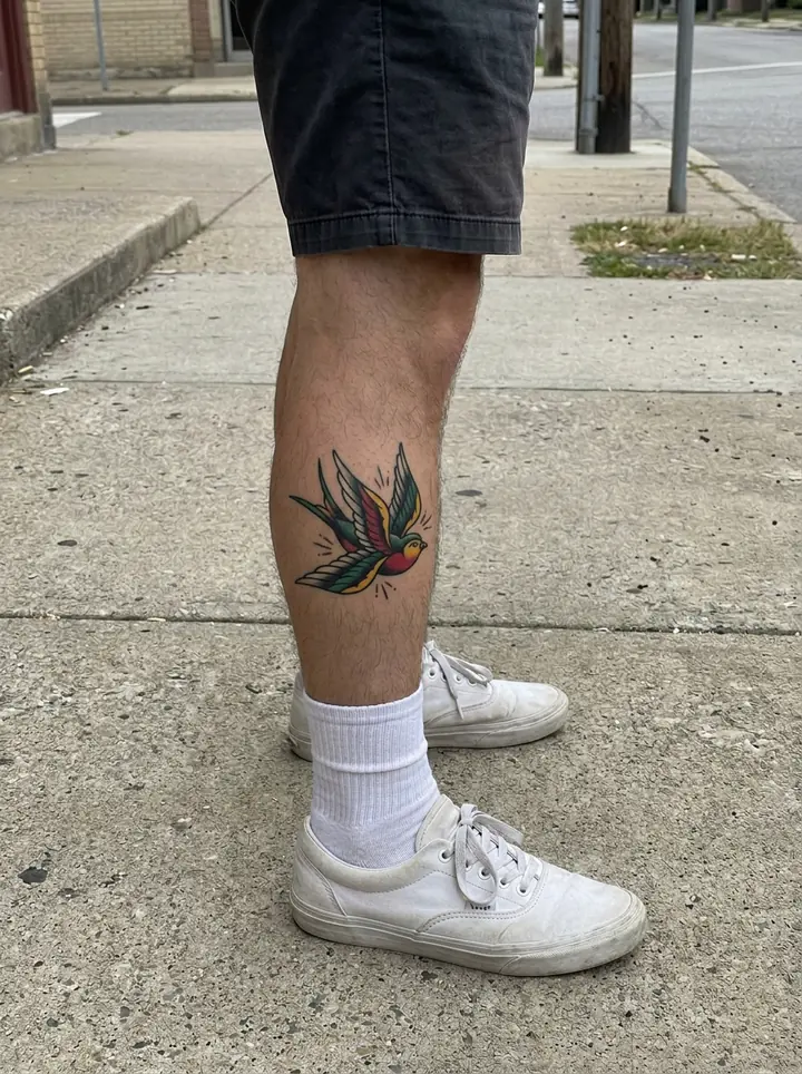 The same leg with the traditional swallow as a palm-sized healed color tattoo on the side of the calf