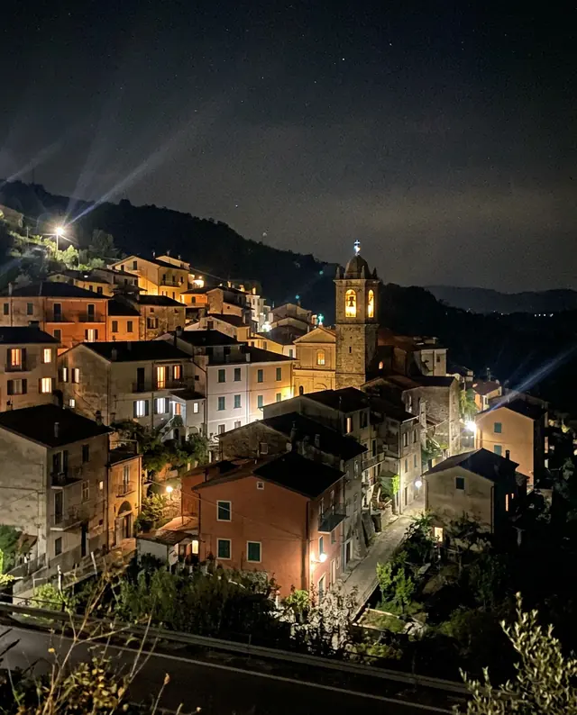 A phone photo of a small hillside town at night with lit windows and a church tower (made with the model)